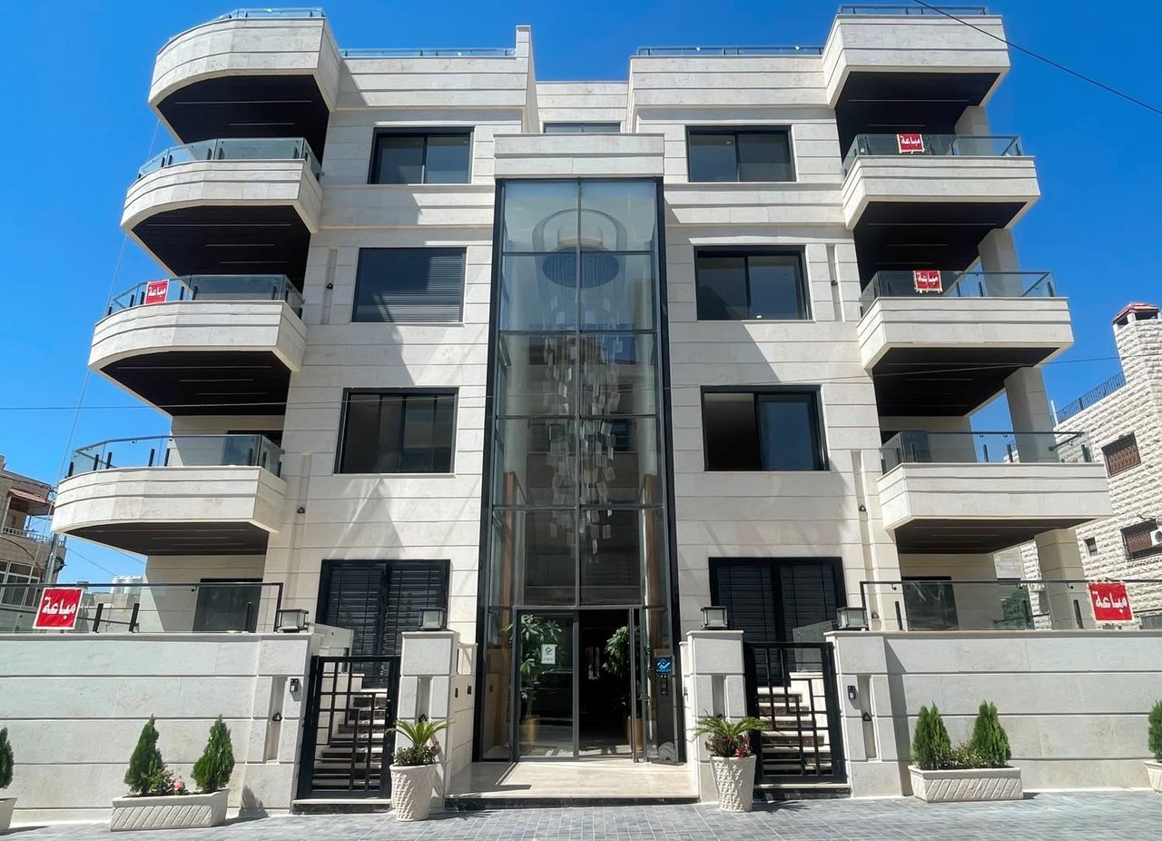 The front elevation of a completed building — stone facing, curved balconies and a full-height glazed entrance.