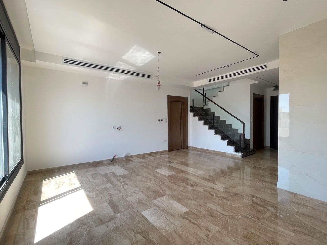 An empty reception with a stone staircase rising to the floor above, marble floor and a recessed ceiling.